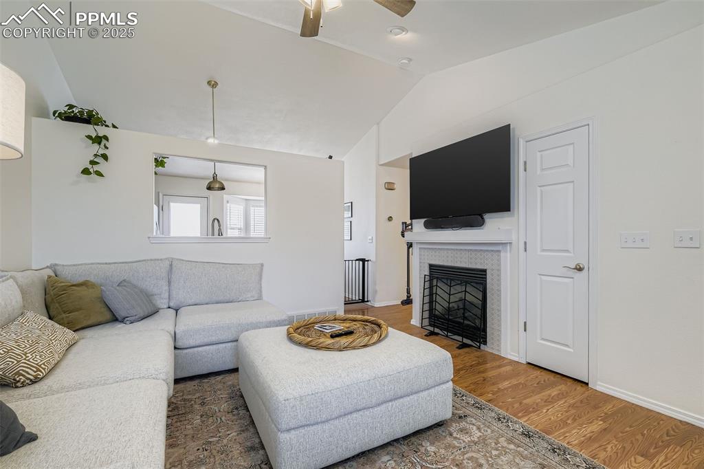 Living room with wood finished floors, a fireplace, vaulted ceiling, and ceiling fan