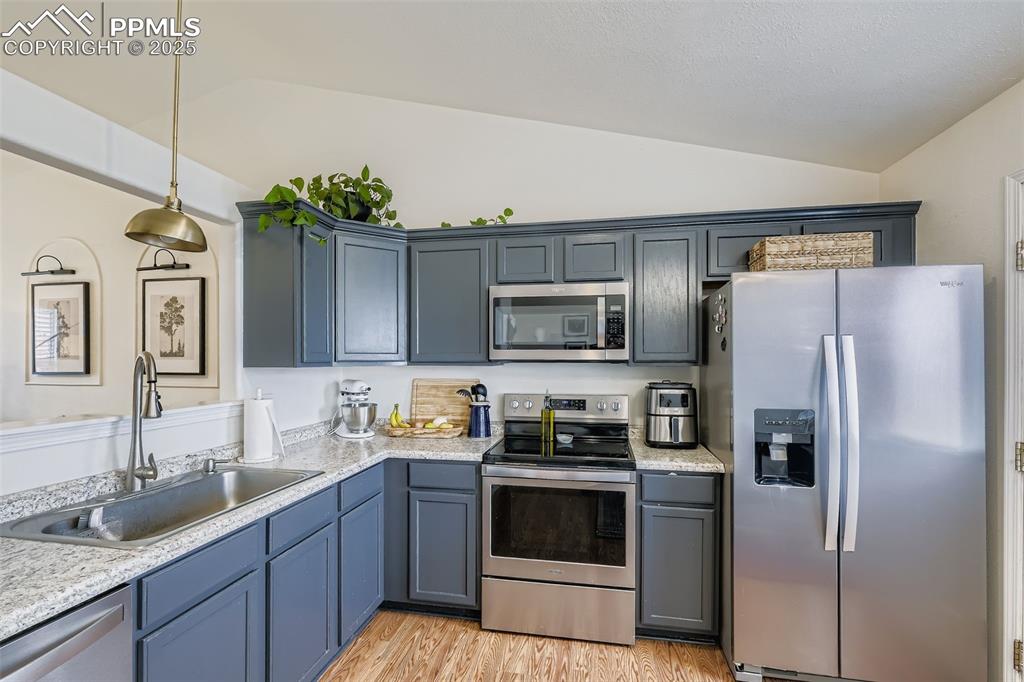 Kitchen featuring appliances with stainless steel finishes, light wood finished floors, hanging light fixtures, lofted ceiling, and gray cabinetry
