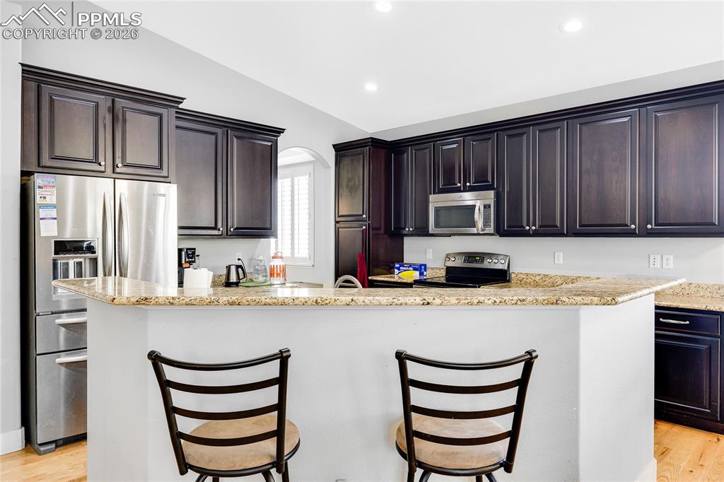 Kitchen featuring light wood-style flooring, lofted ceiling, stainless steel appliances, light stone counters, and arched walkways