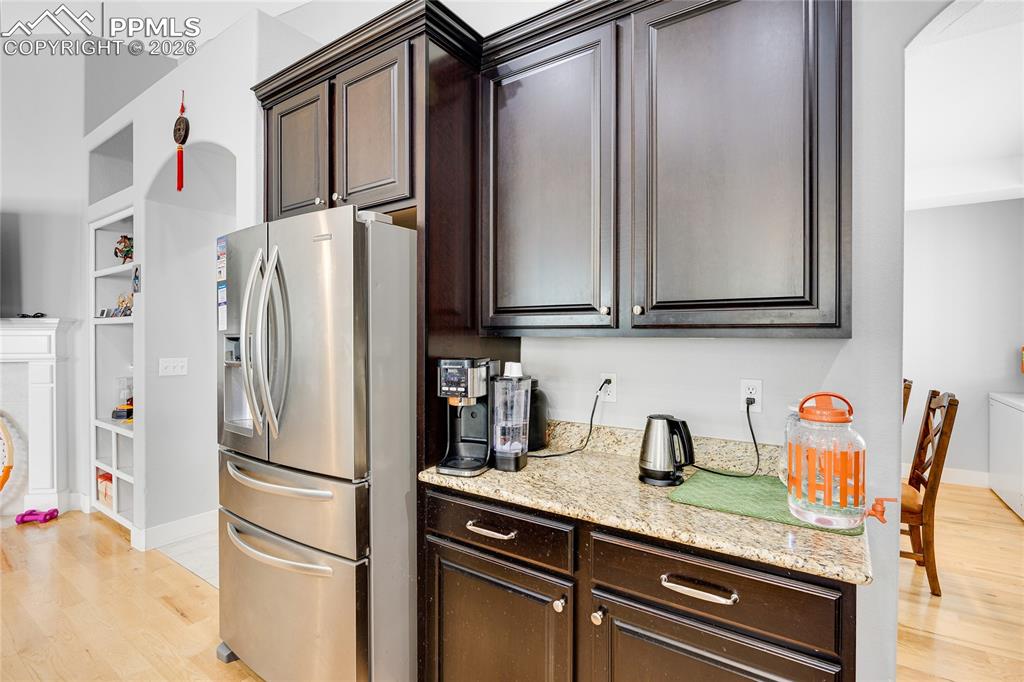 Kitchen featuring dark wood finish cabinetry, stainless steel fridge with ice dispenser, light stone counters, and built in features