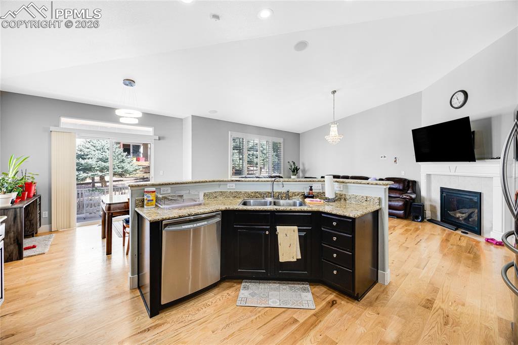 Kitchen with dark cabinets, open floor plan, a kitchen island with sink, a glass covered fireplace, and stainless steel appliances