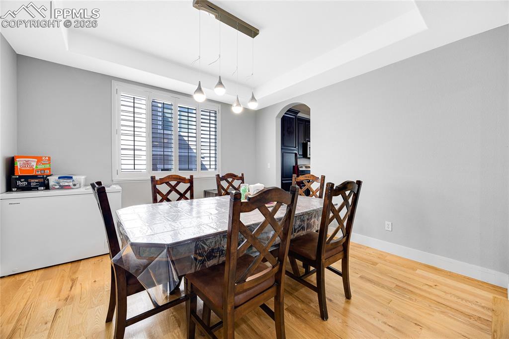Dining space with a tray ceiling, arched walkways, and light wood-style floors