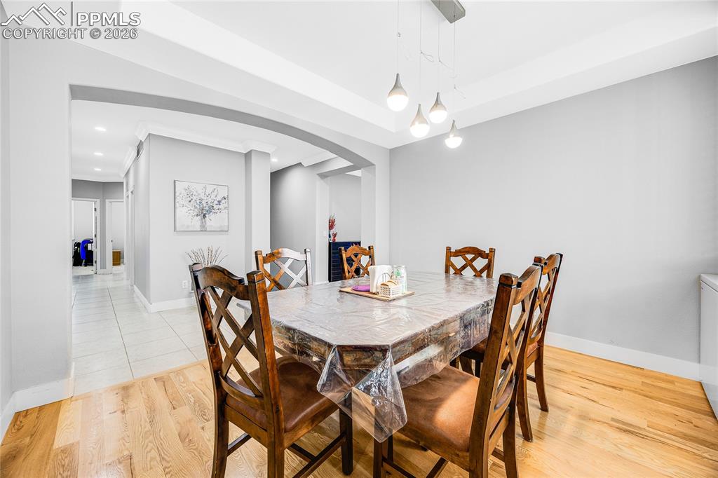 Dining room featuring light wood-style floors, arched walkways, recessed lighting, and a tray ceiling