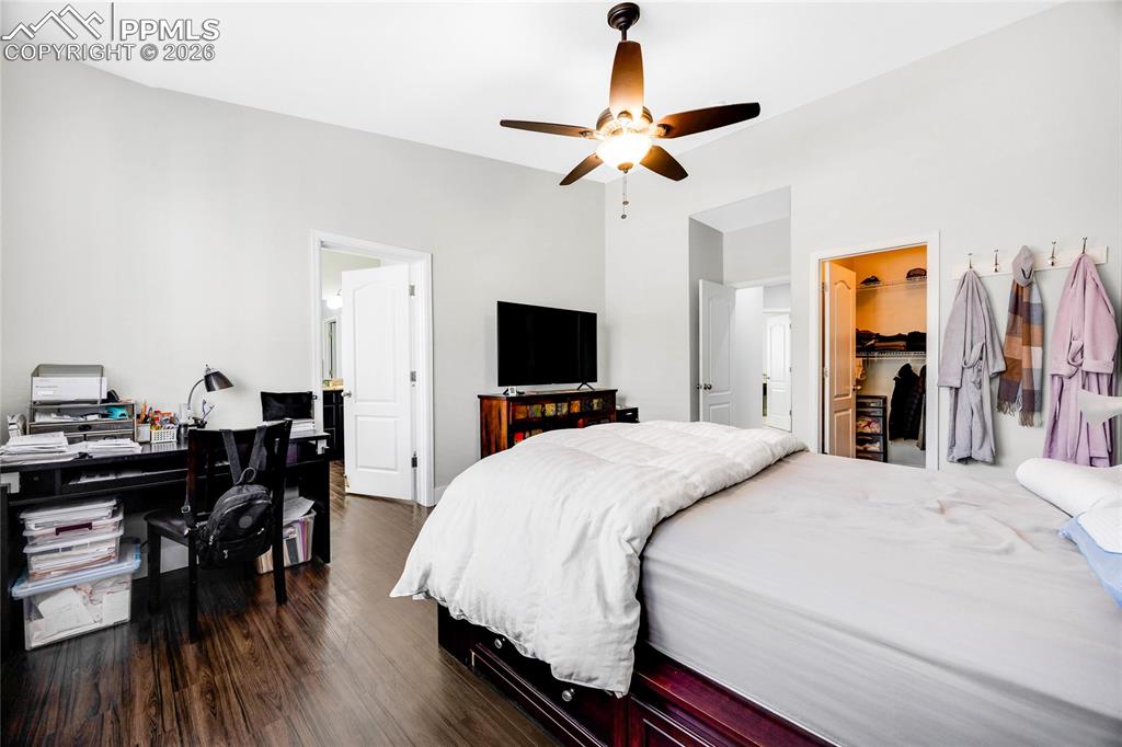 Bedroom featuring an office area, a spacious closet, dark wood-style flooring, ceiling fan, and connected bathroom