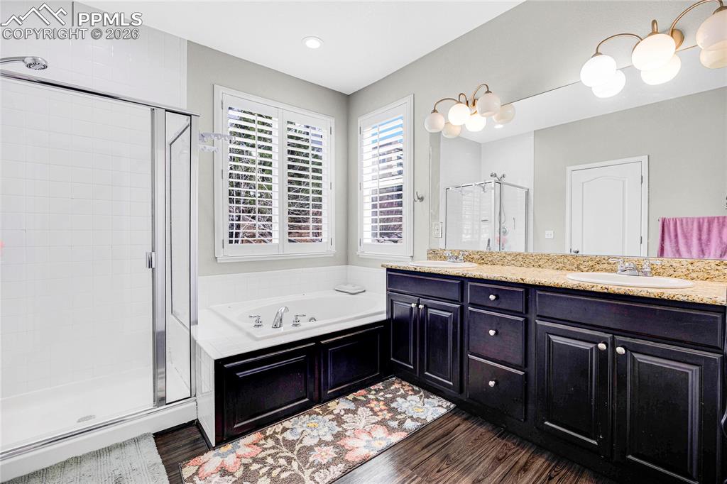 Full bathroom featuring a stall shower, double vanity, dark wood-style floors, and a bath