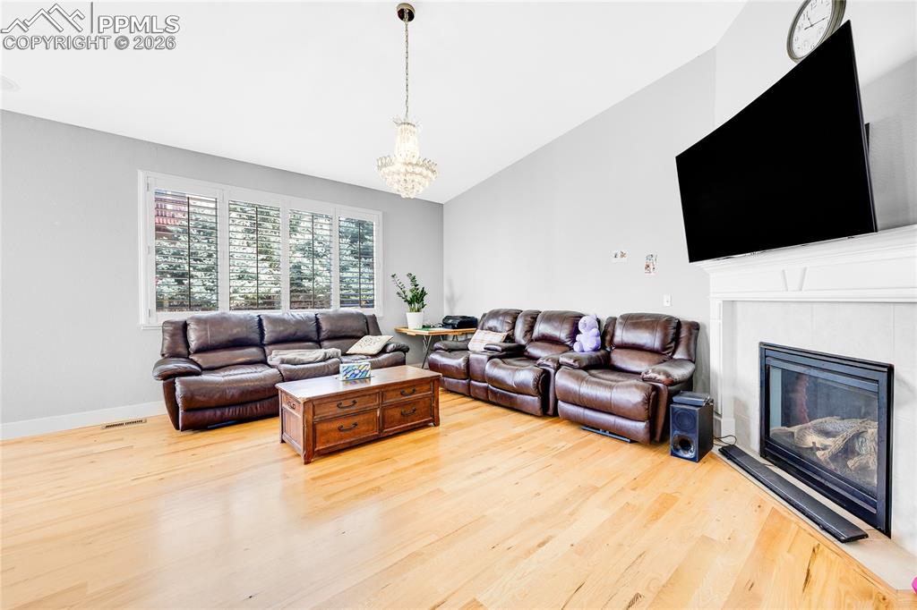 Living room featuring light wood-style floors, hanging lights, lofted ceiling, and a glass covered fireplace