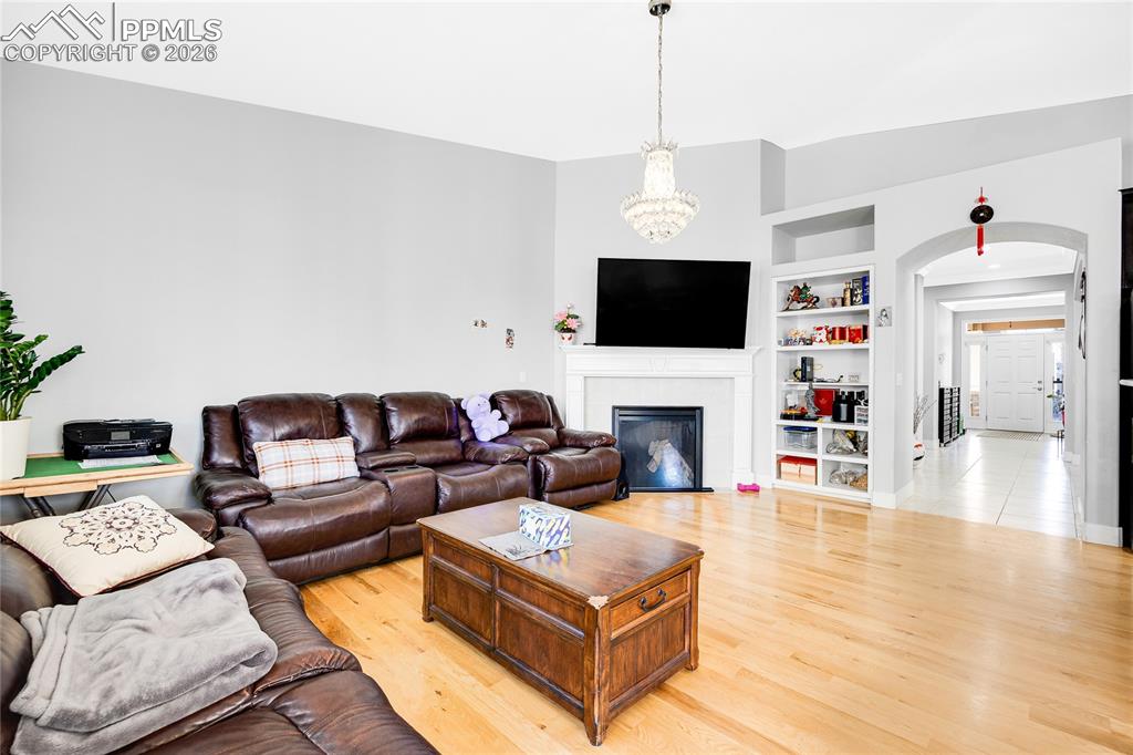 Living room featuring built in shelves, light wood-style flooring, a chandelier, a glass covered fireplace, and arched walkways