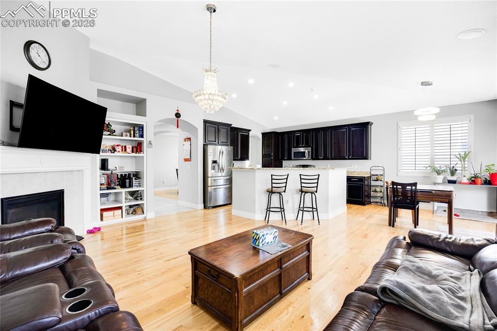 Living room with arched walkways, built in shelves, vaulted ceiling, a tile fireplace, and light wood finished floors