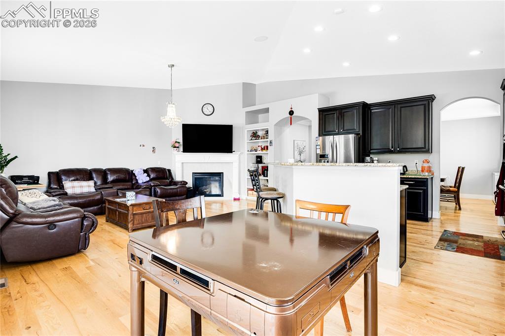 Dining area featuring arched walkways, light wood-style flooring, a glass covered fireplace, and vaulted ceiling