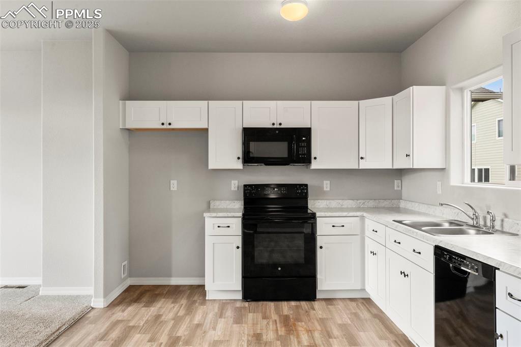 Kitchen featuring black appliances, white cabinets, light countertops, and light wood finished floors