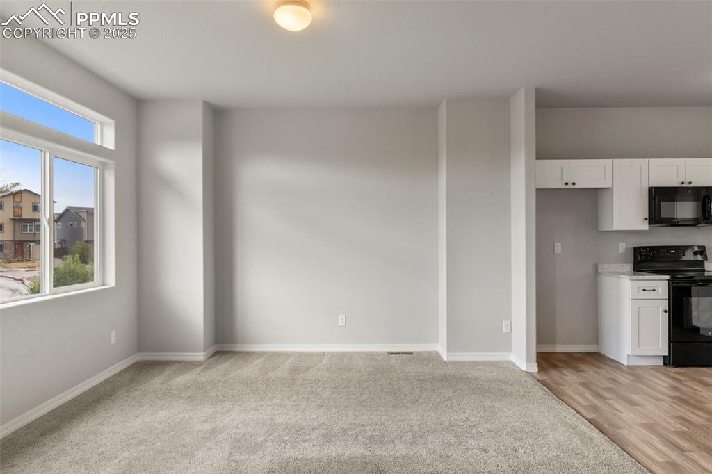 Unfurnished living room featuring baseboards and light carpet