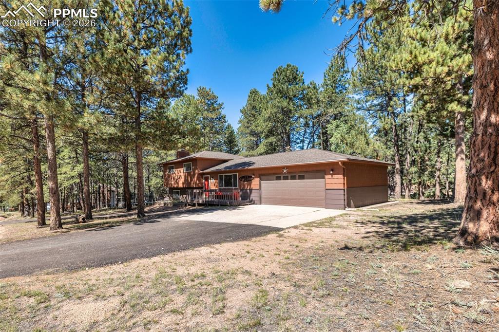 View of front of home with an attached garage, driveway, view of wooded area, and a chimney