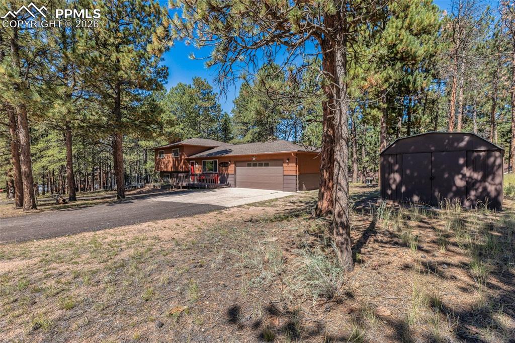 Tri-level home with a garage, concrete driveway, view of wooded area, and a storage shed