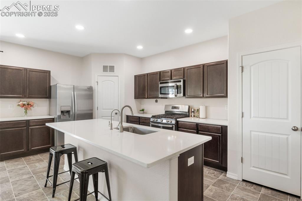 Kitchen with dark brown cabinetry, appliances with stainless steel finishes, a breakfast bar, an island with sink, and recessed lighting