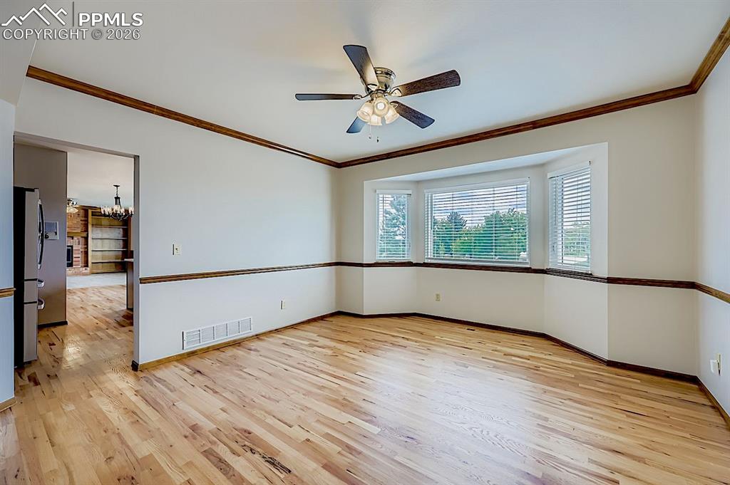 Unfurnished room featuring crown molding, a chandelier, light wood-type flooring, and a ceiling fan