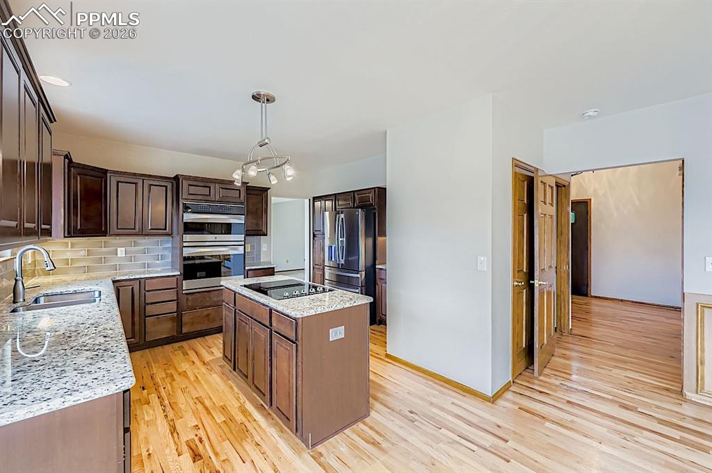 Kitchen featuring backsplash, a kitchen island, light wood-type flooring, light stone countertops, and stainless steel appliances