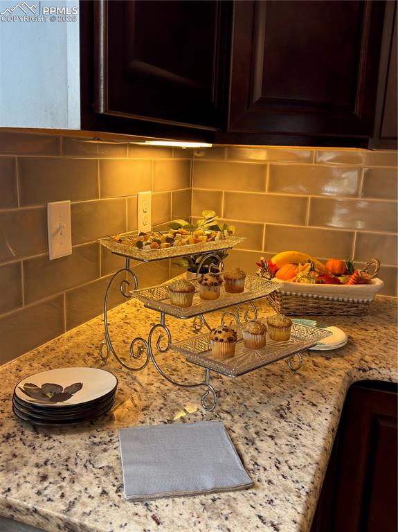 Detailed view of decorative backsplash, dark brown cabinetry, and light stone countertops
