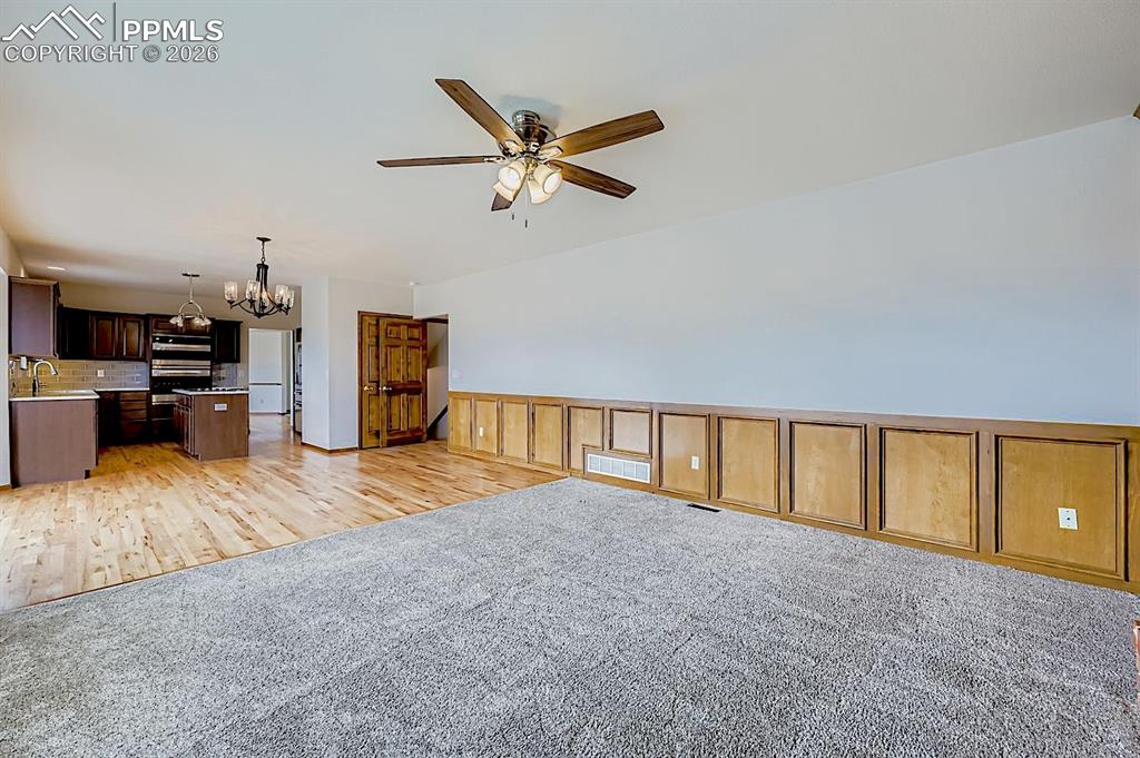 Unfurnished living room with a chandelier, light wood-style floors, light carpet, and a ceiling fan