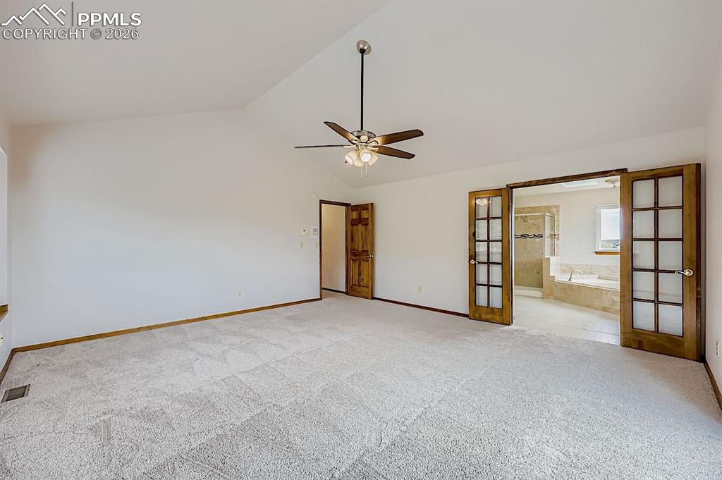 Unfurnished bedroom with vaulted ceiling, ceiling fan, light carpet, french doors, and connected bathroom