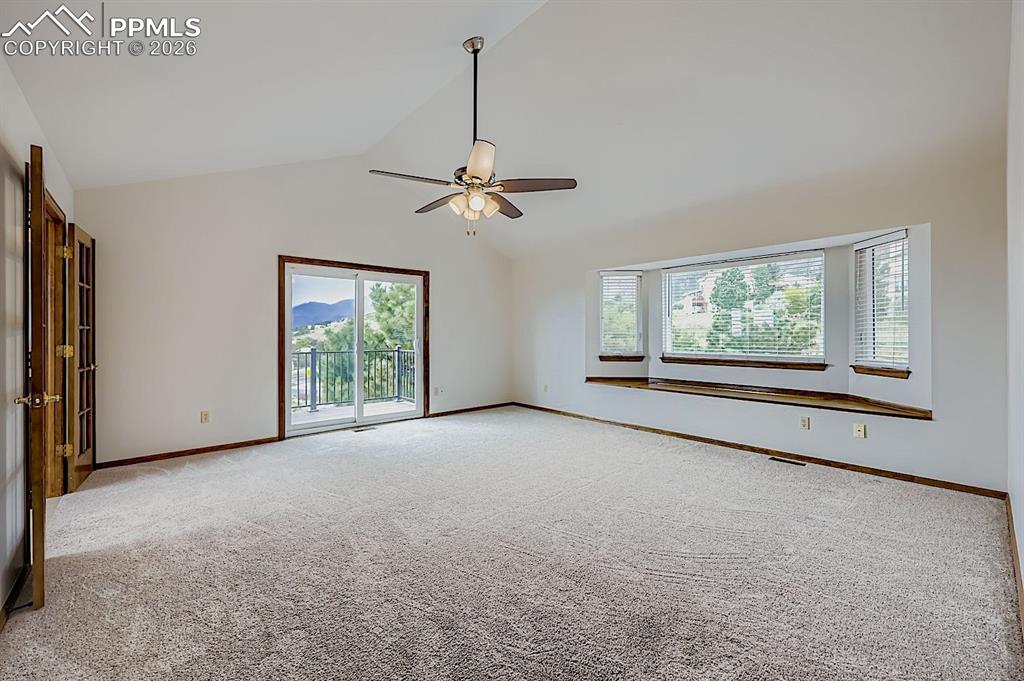 Empty room with light colored carpet, high vaulted ceiling, and ceiling fan