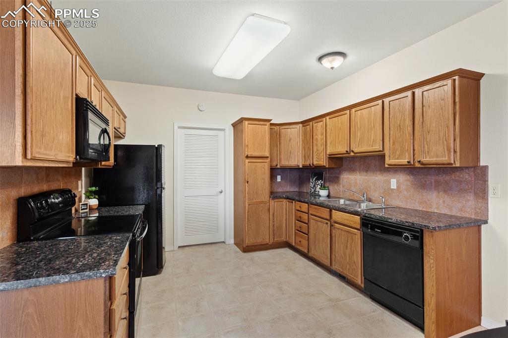 Kitchen featuring tasteful backsplash, black appliances, dark stone counters, brown cabinetry, and light flooring