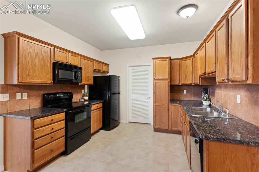 Kitchen with backsplash, black appliances, dark stone countertops, and brown cabinetry
