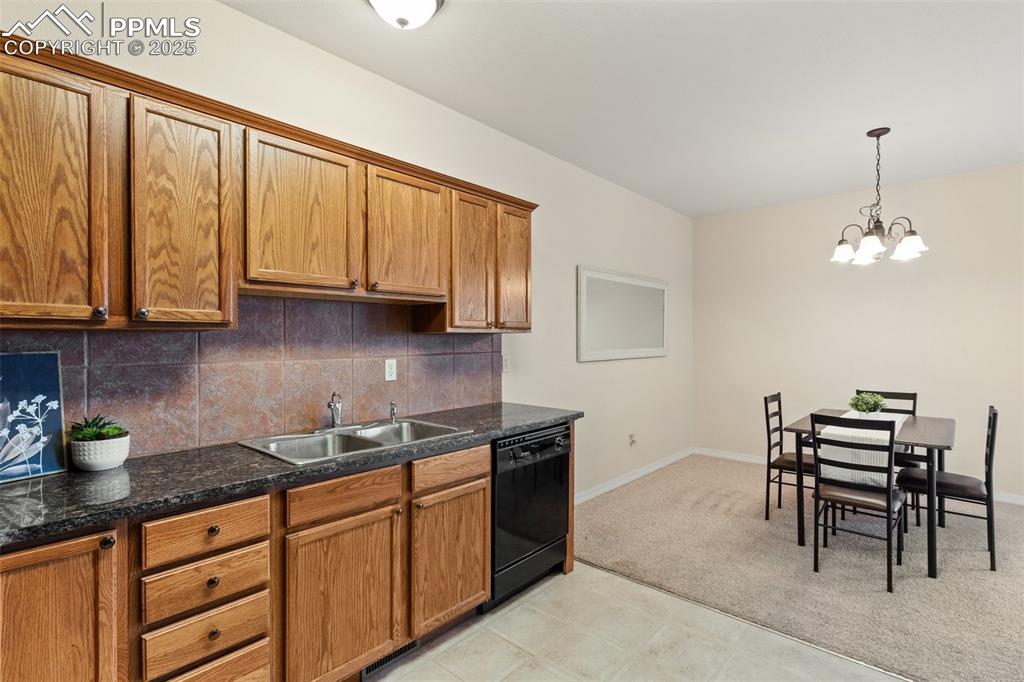Kitchen featuring backsplash, brown cabinetry, light carpet, and black dishwasher