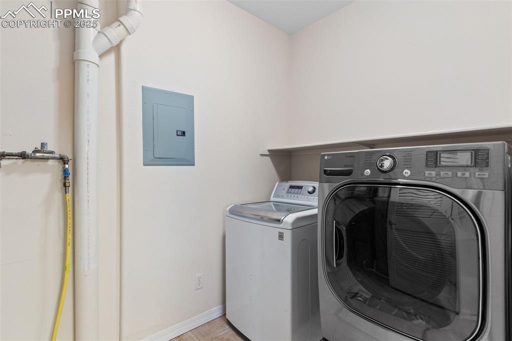 Laundry room with electric panel, washing machine and dryer, and light tile patterned floors
