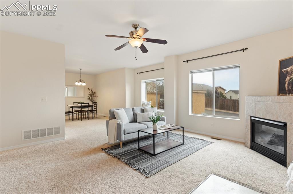 Living area featuring a fireplace, carpet flooring, a ceiling fan, and a chandelier