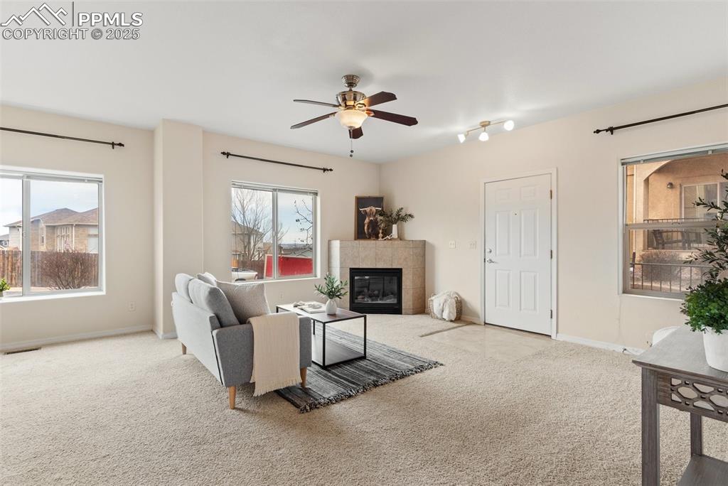 Living area with a tile fireplace, carpet, and ceiling fan