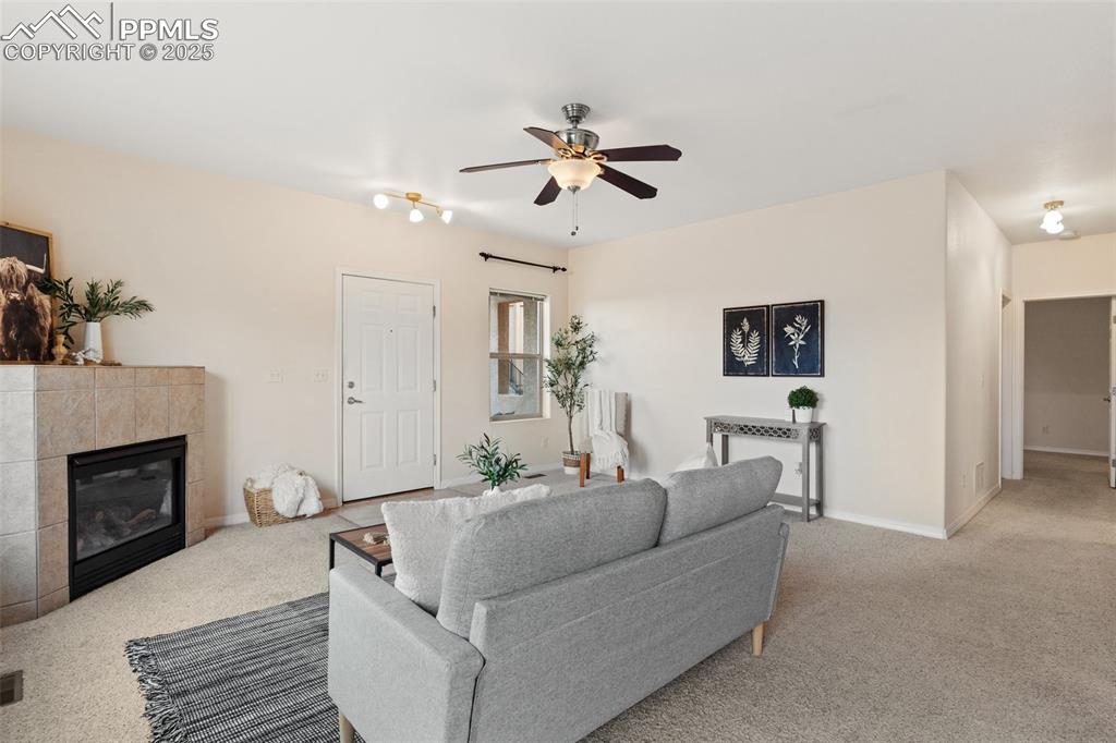 Carpeted living area with a tiled fireplace and ceiling fan