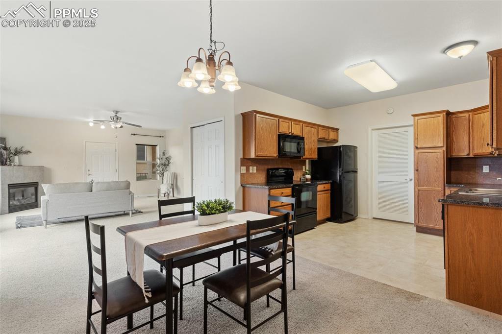 Dining room featuring light colored carpet, a chandelier, a fireplace, and a ceiling fan