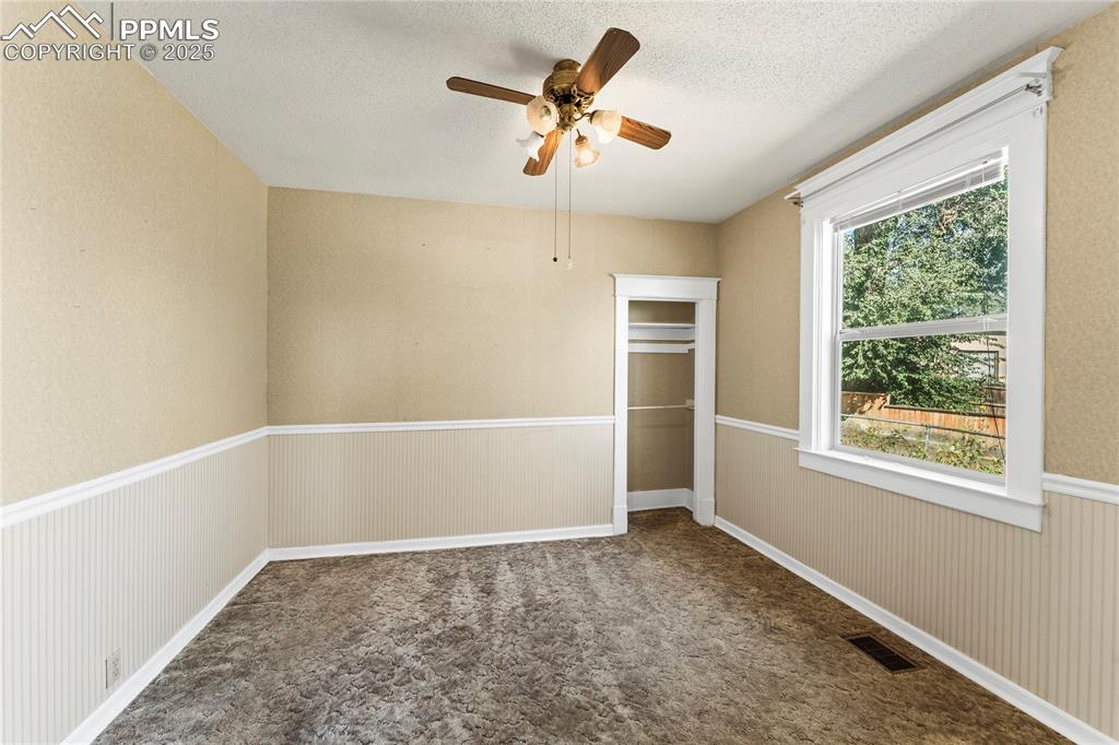Unfurnished bedroom with a closet, dark colored carpet, a wainscoted wall, ceiling fan, and a textured ceiling