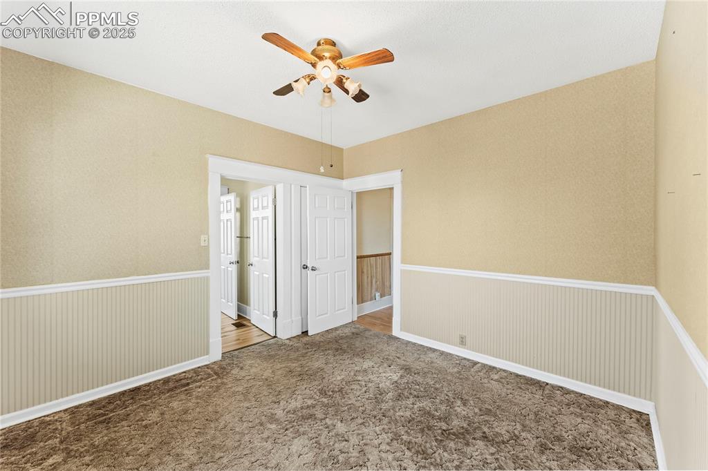 Spare room featuring carpet flooring, ceiling fan, wainscoting, and wallpapered walls