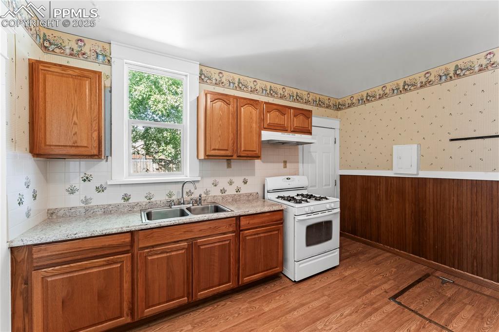 Kitchen with wallpapered walls, white gas stove, light wood finished floors, brown cabinetry, and light countertops