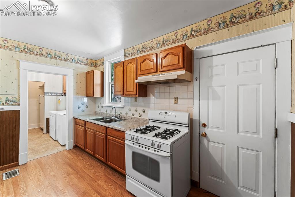 Kitchen featuring white gas stove, brown cabinetry, light countertops, light wood-style flooring, and wallpapered walls