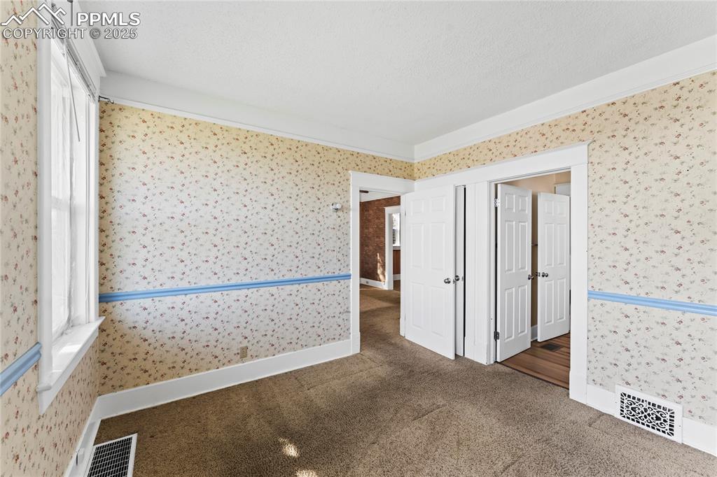 Spare room with wallpapered walls, carpet floors, and a textured ceiling
