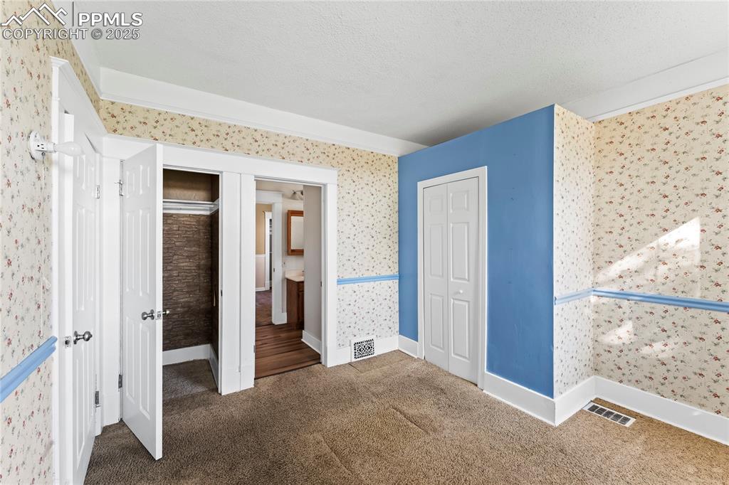 Unfurnished bedroom featuring wallpapered walls, carpet floors, a closet, and a textured ceiling