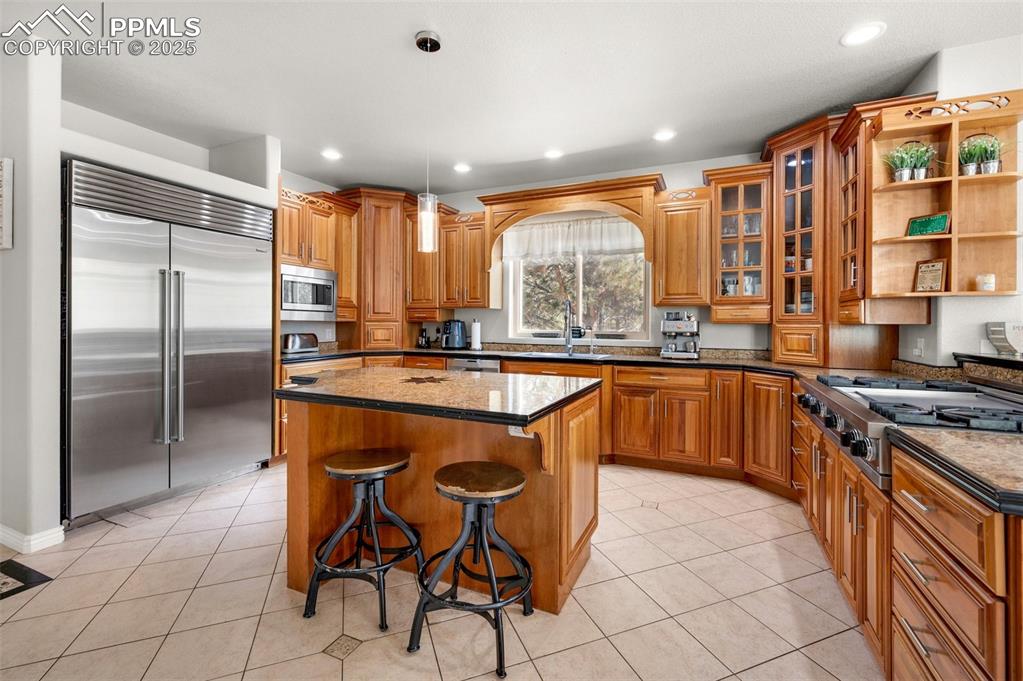 Kitchen featuring light tile patterned floors, built in appliances, brown cabinets, and a center island