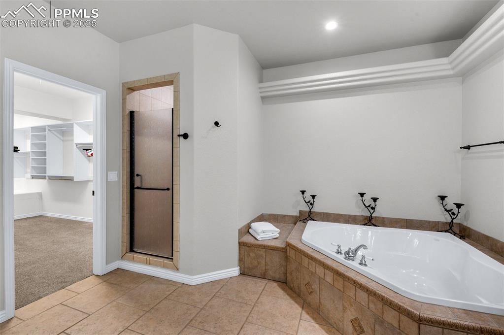 Bathroom featuring a garden tub, a stall shower, tile patterned flooring, baseboards, and a spacious closet
