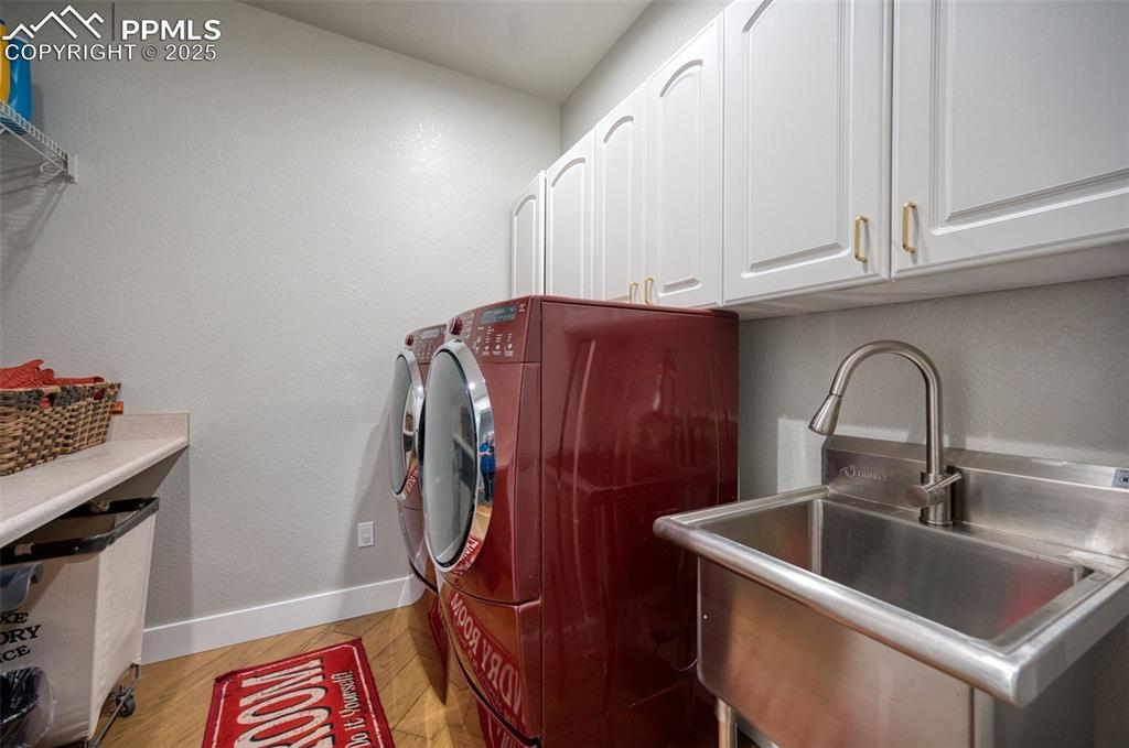 Laundry area with baseboards, washing machine and dryer, light wood-type flooring, cabinet space, and a sink
