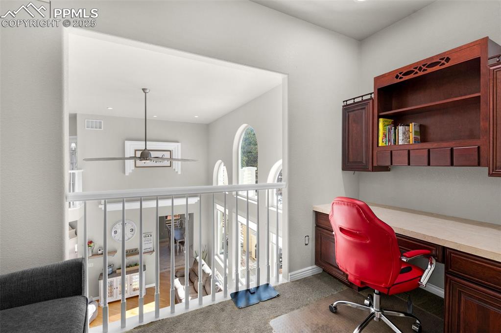 Carpeted office featuring visible vents, baseboards, a ceiling fan, and built in desk