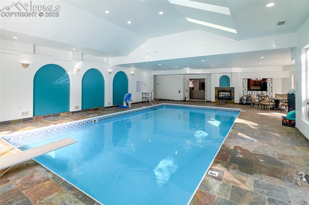 Indoor pool featuring a skylight, arched walkways, and a diving board
