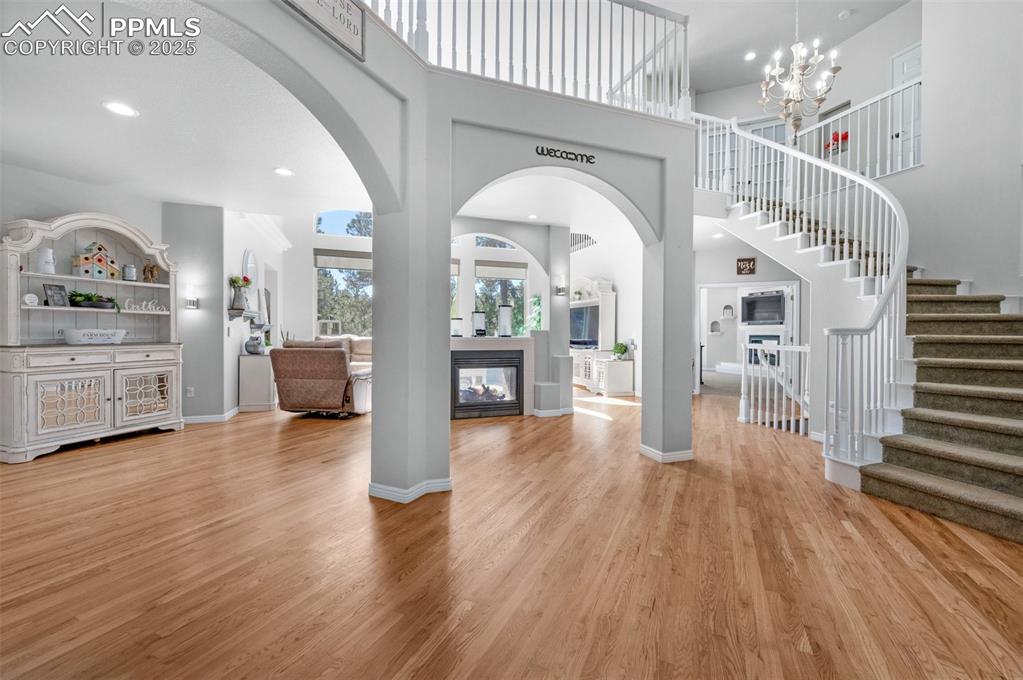 Foyer entrance with stairway, light wood finished floors, a multi sided fireplace, a towering ceiling, and a notable chandelier