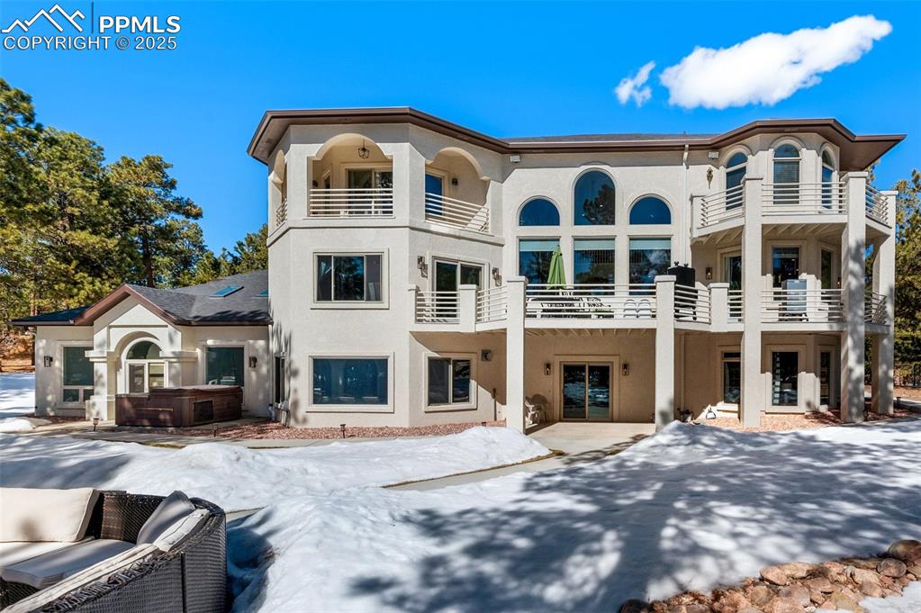 Snow covered back of property featuring stucco siding, a patio area, a balcony, and a hot tub
