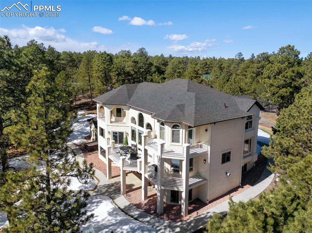 Rear view of property featuring a forest view, roof with shingles, stucco siding, a balcony, and a patio