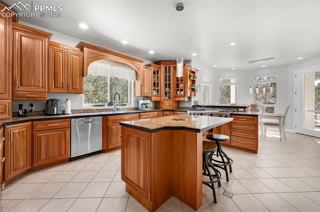 Kitchen featuring light tile patterned floors, stainless steel dishwasher, a peninsula, and brown cabinetry