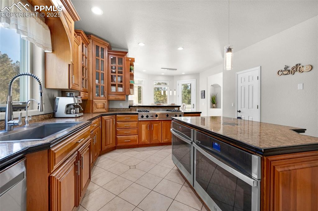 Kitchen with pendant lighting, a sink, appliances with stainless steel finishes, brown cabinetry, and glass insert cabinets