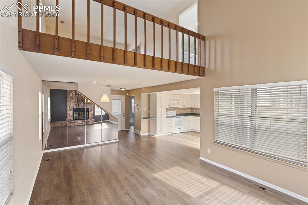 Living room with light wood-type flooring, a stone fireplace, and a high ceiling