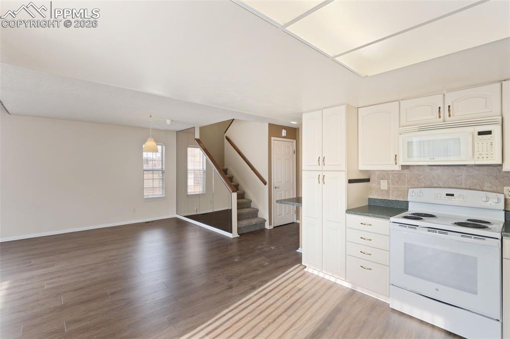 Kitchen with white appliances, tasteful backsplash, wood-style floors, white cabinetry, and open floor plan